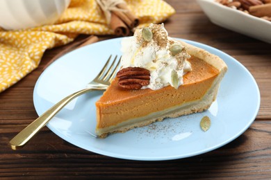 Photo of Piece of tasty homemade pumpkin pie with whipped cream, seeds and pecan nut on wooden table, closeup