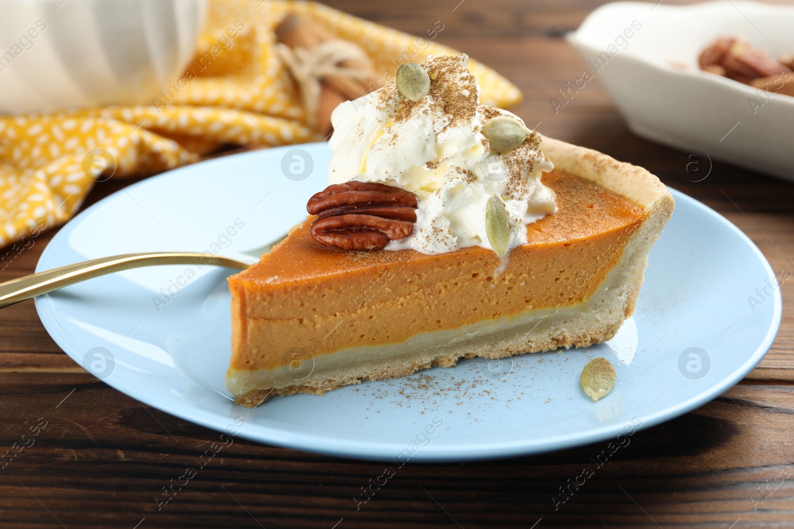 Photo of Piece of tasty homemade pumpkin pie with whipped cream, seeds and pecan nut on wooden table, closeup