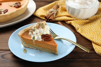 Piece of tasty homemade pumpkin pie with whipped cream, seeds and pecan nut on wooden table, closeup