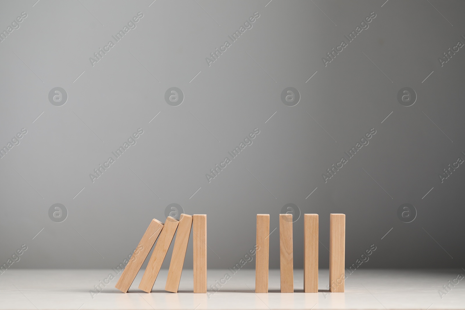 Photo of Domino effect. Wooden blocks falling on white table. Space for text