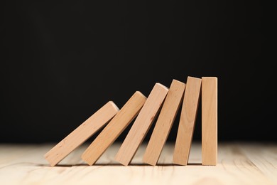 Photo of Domino effect. Blocks falling on wooden table, closeup