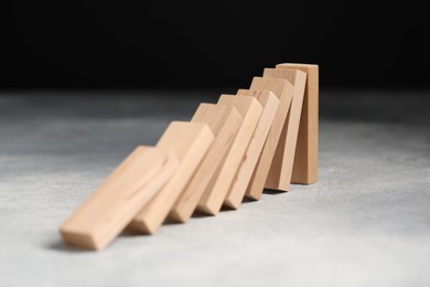 Photo of Domino effect. Wooden blocks falling on grey table, closeup