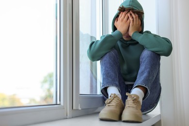 Loneliness concept. Sad teenage boy on windowsill indoors