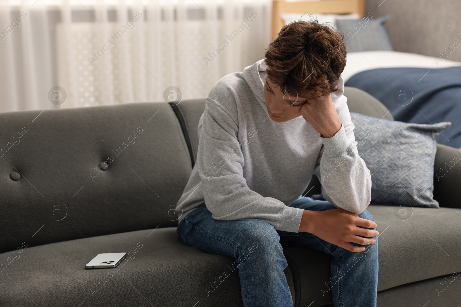 Photo of Loneliness concept. Sad teenage boy with smartphone on sofa at home