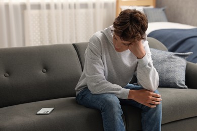 Loneliness concept. Sad teenage boy with smartphone on sofa at home