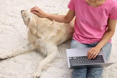 Photo of Online pet shop. Woman with laptop making order for cute Golden Retriever dog on rug at home, closeup