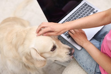 Photo of Online pet shop. Woman with laptop making order for cute Golden Retriever dog at home, closeup