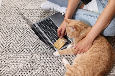 Photo of Online pet shop. Woman with laptop, credit card and cute cat making order on rug at home, closeup