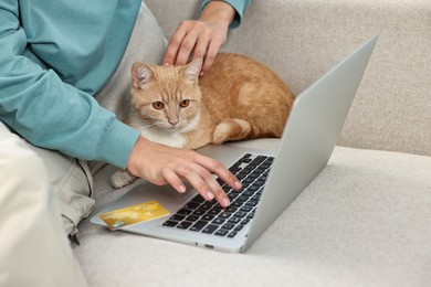 Photo of Online pet shop. Woman with laptop, credit card and cute cat making order on sofa at home, closeup