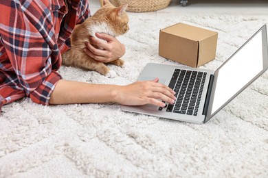 Photo of Online pet shop. Woman with laptop making order and cute cat on rug at home, closeup