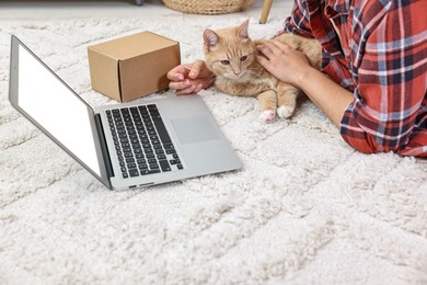 Online pet shop. Woman with laptop making order and cute cat on rug at home, closeup