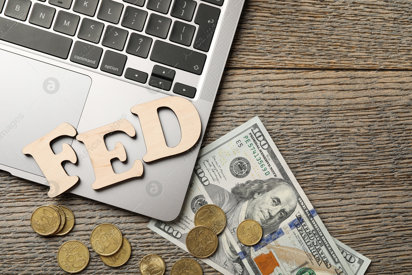 Photo of Letters Fed (Federal Reserve System), coins, dollar banknotes and laptop on wooden table, flat lay