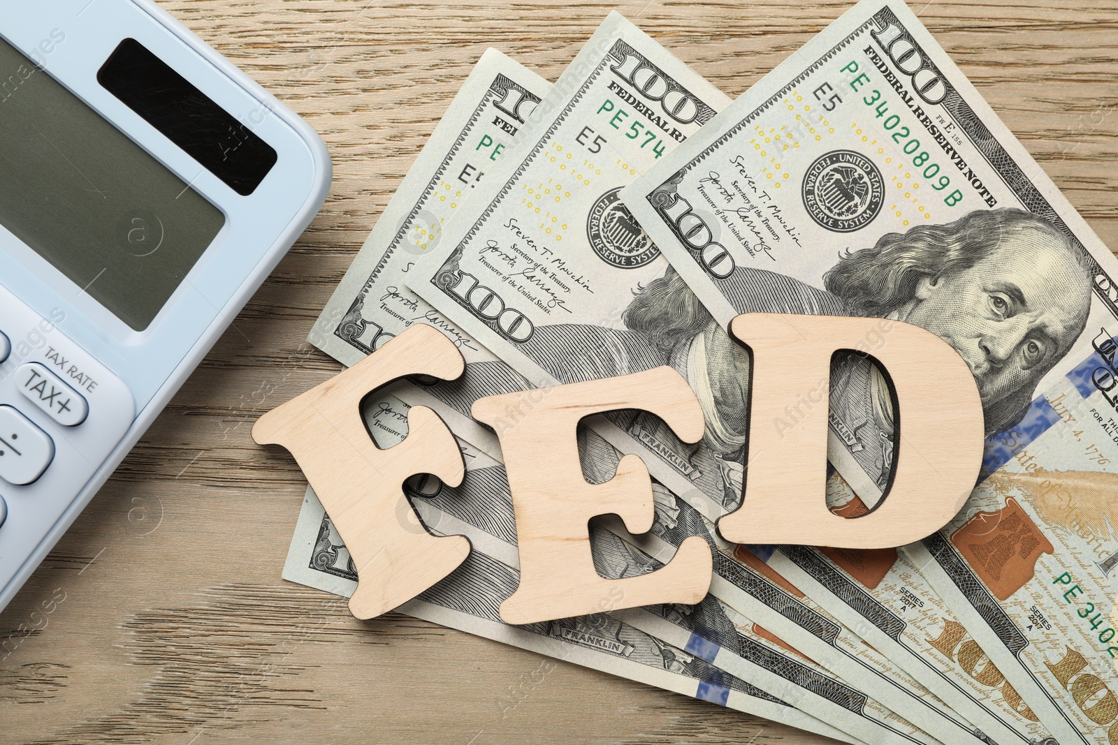 Photo of Letters Fed (Federal Reserve System), calculator and dollar banknotes on wooden table, flat lay