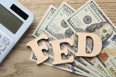 Photo of Letters Fed (Federal Reserve System), calculator and dollar banknotes on wooden table, flat lay