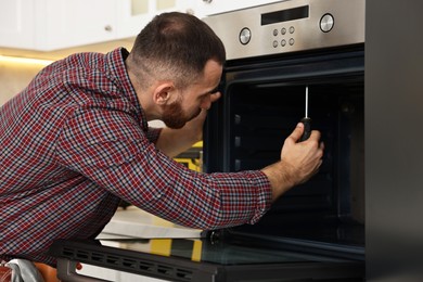 Repairman with screwdriver fixing oven in kitchen