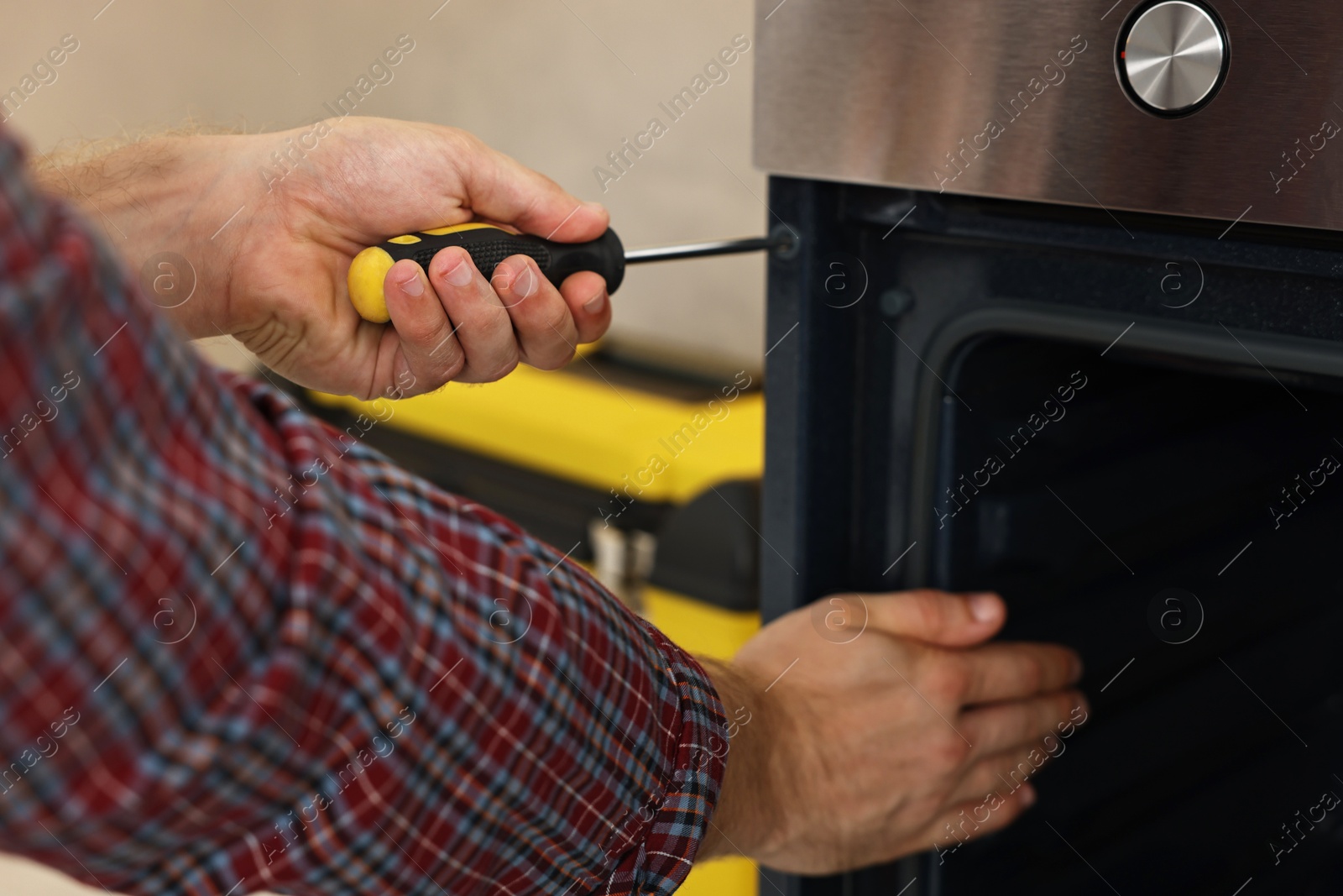 Photo of Repairman with screwdriver fixing oven indoors, closeup