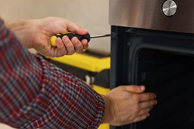 Photo of Repairman with screwdriver fixing oven indoors, closeup