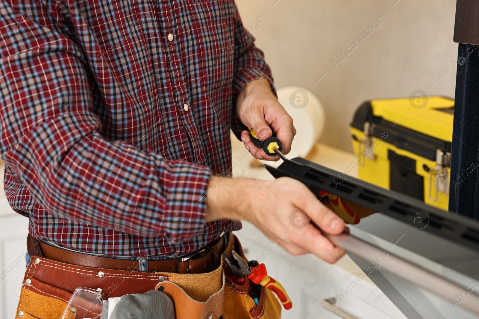 Photo of Repairman with screwdriver fixing oven indoors, closeup