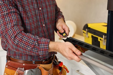 Repairman with screwdriver fixing oven indoors, closeup