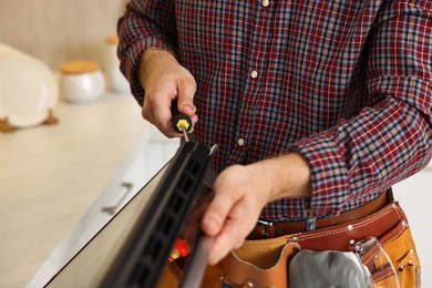 Repairman with screwdriver fixing oven indoors, closeup