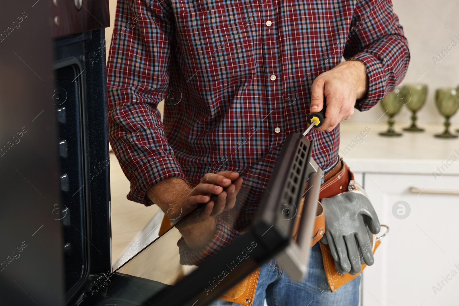 Photo of Repairman with screwdriver fixing oven indoors, closeup