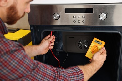 Photo of Repairman testing oven element with multimeter, closeup