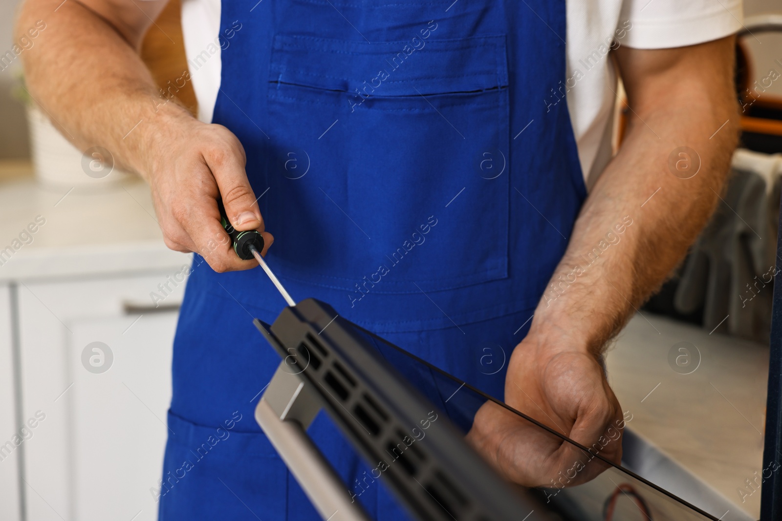 Photo of Repairman with screwdriver fixing oven indoors, closeup