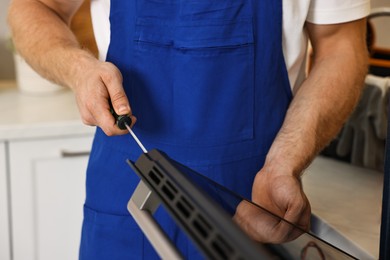 Repairman with screwdriver fixing oven indoors, closeup