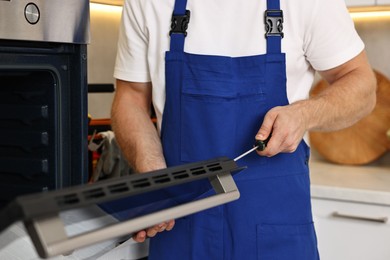 Photo of Repairman with screwdriver fixing oven indoors, closeup