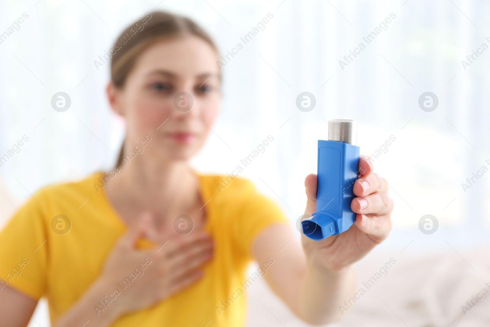 Photo of Woman holding asthma inhaler indoors, selective focus