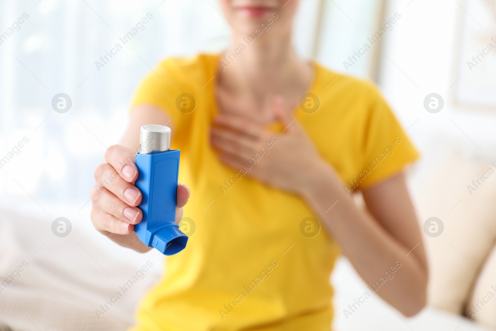 Photo of Woman holding asthma inhaler indoors, selective focus