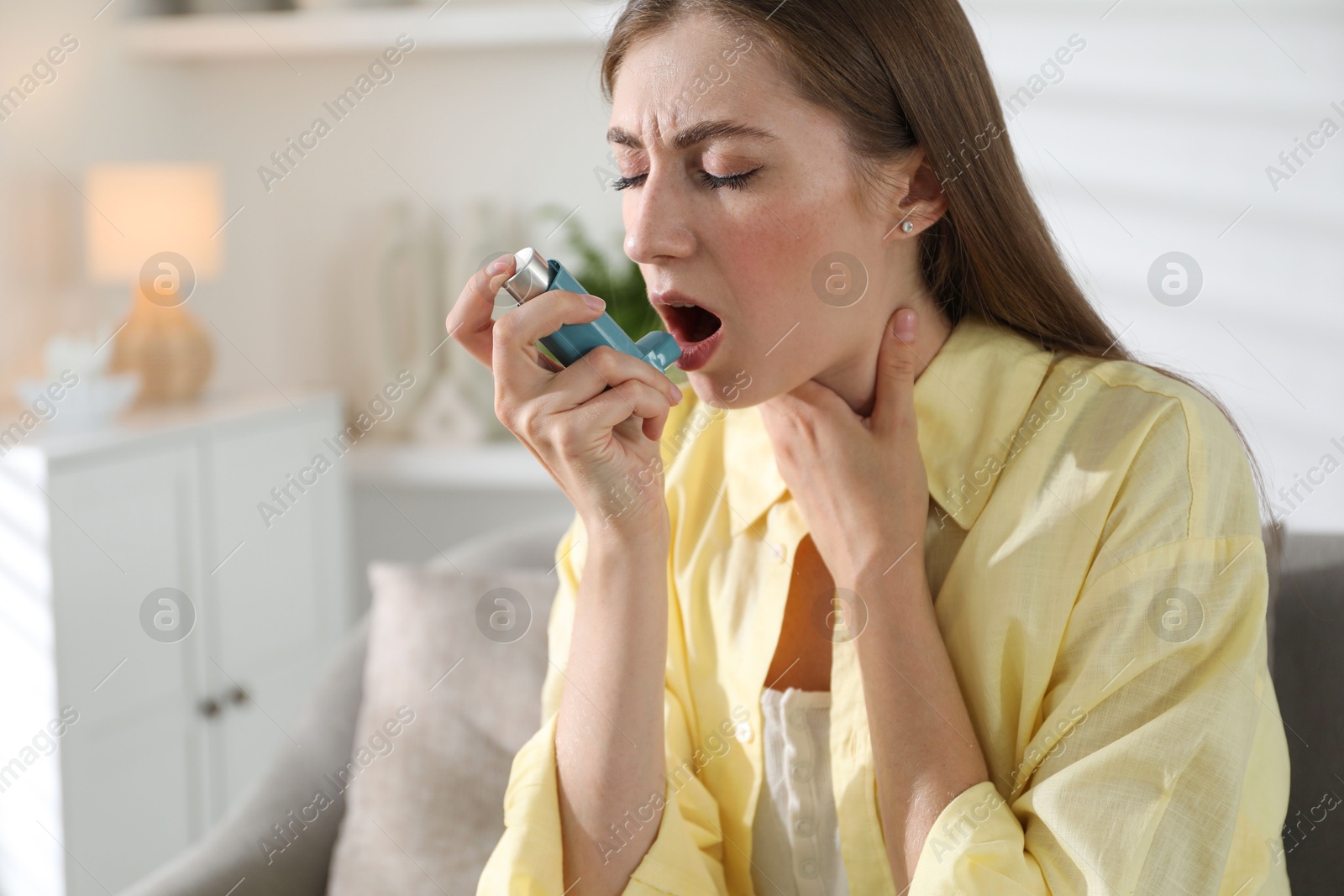 Photo of Young woman using asthma inhaler at home