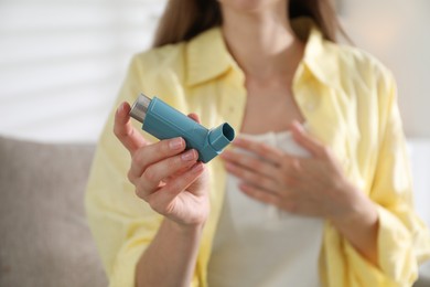 Photo of Woman holding asthma inhaler indoors, selective focus