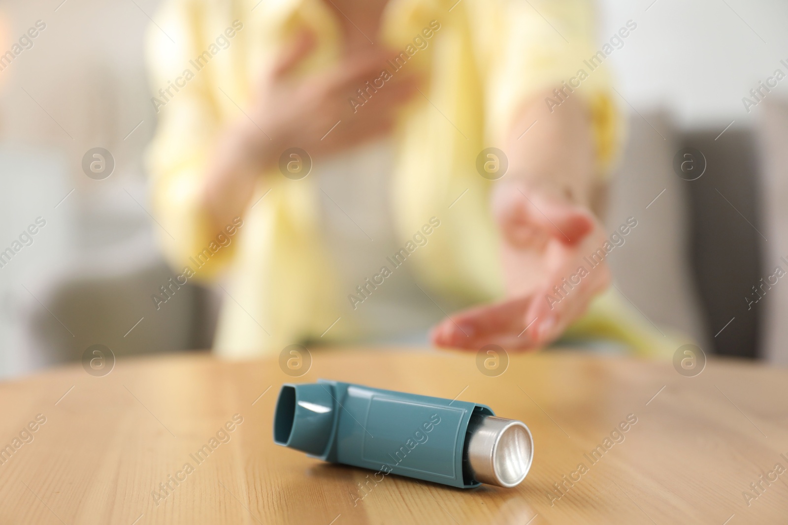 Photo of Young woman with asthma inhaler at table, selective focus