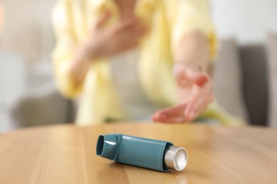 Young woman with asthma inhaler at table, selective focus