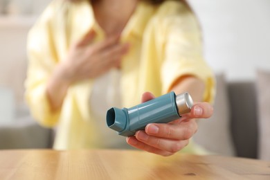 Photo of Young woman with asthma inhaler at table, selective focus