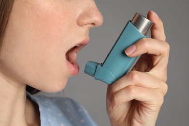 Woman using asthma inhaler on grey background, closeup