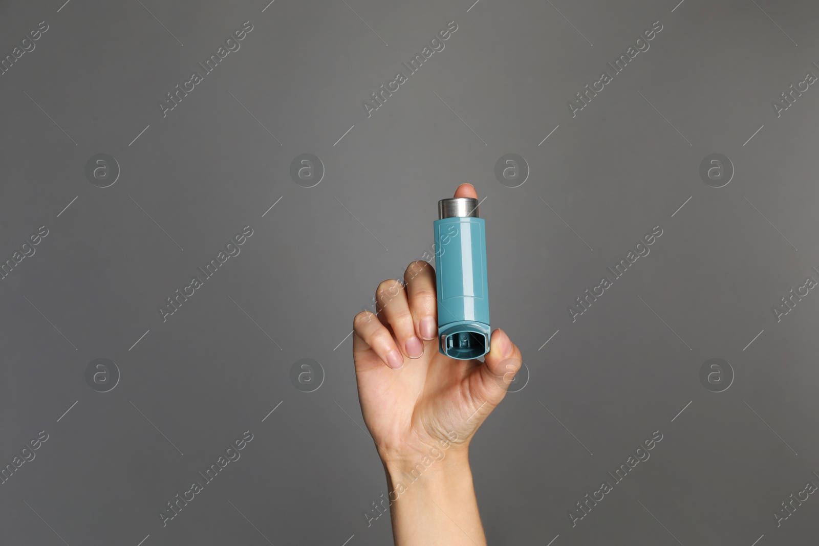 Photo of Woman holding asthma inhaler on grey background, closeup