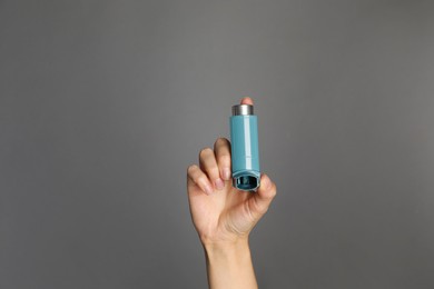 Woman holding asthma inhaler on grey background, closeup