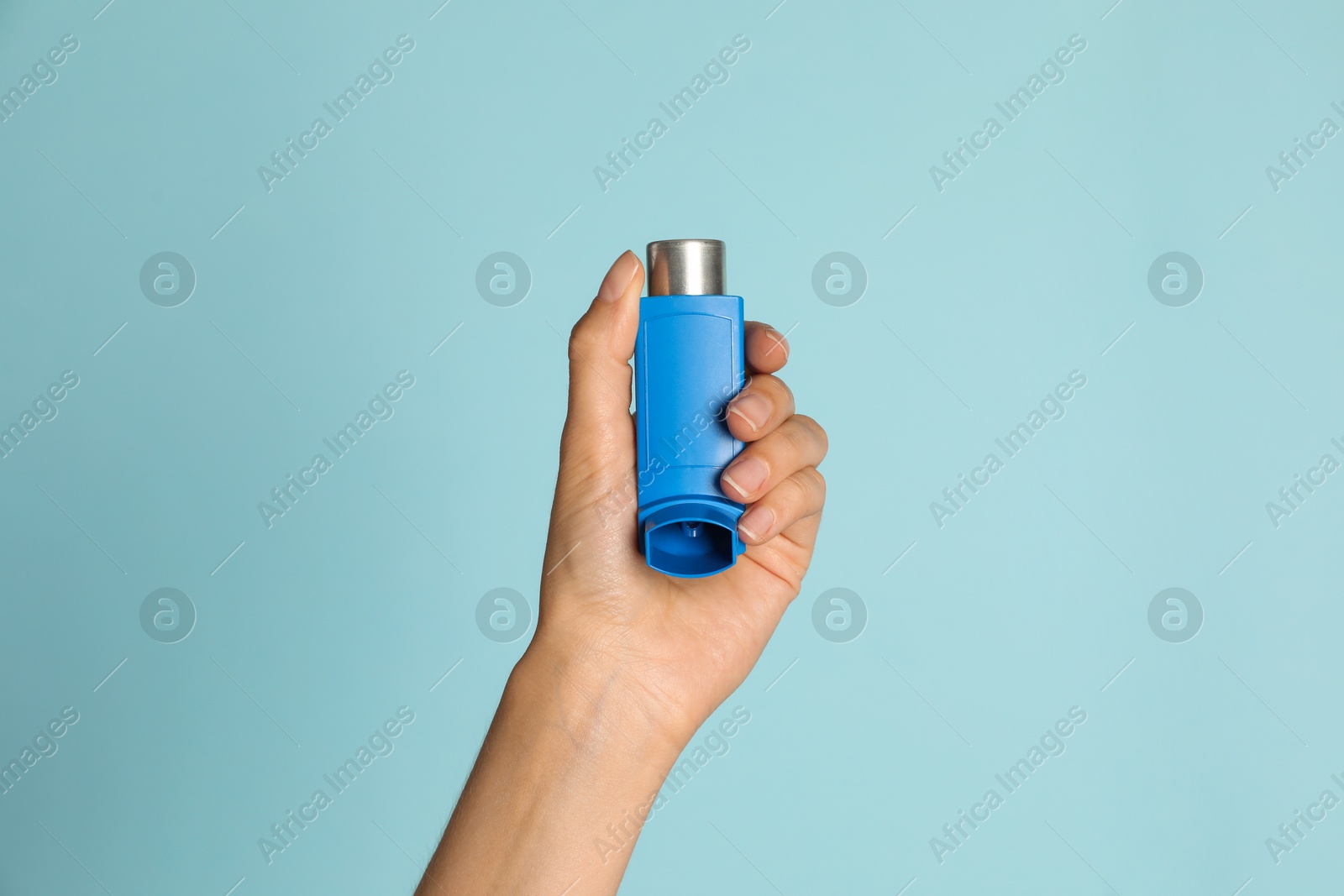 Photo of Woman holding asthma inhaler on light blue background, closeup