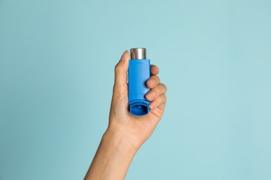 Woman holding asthma inhaler on light blue background, closeup