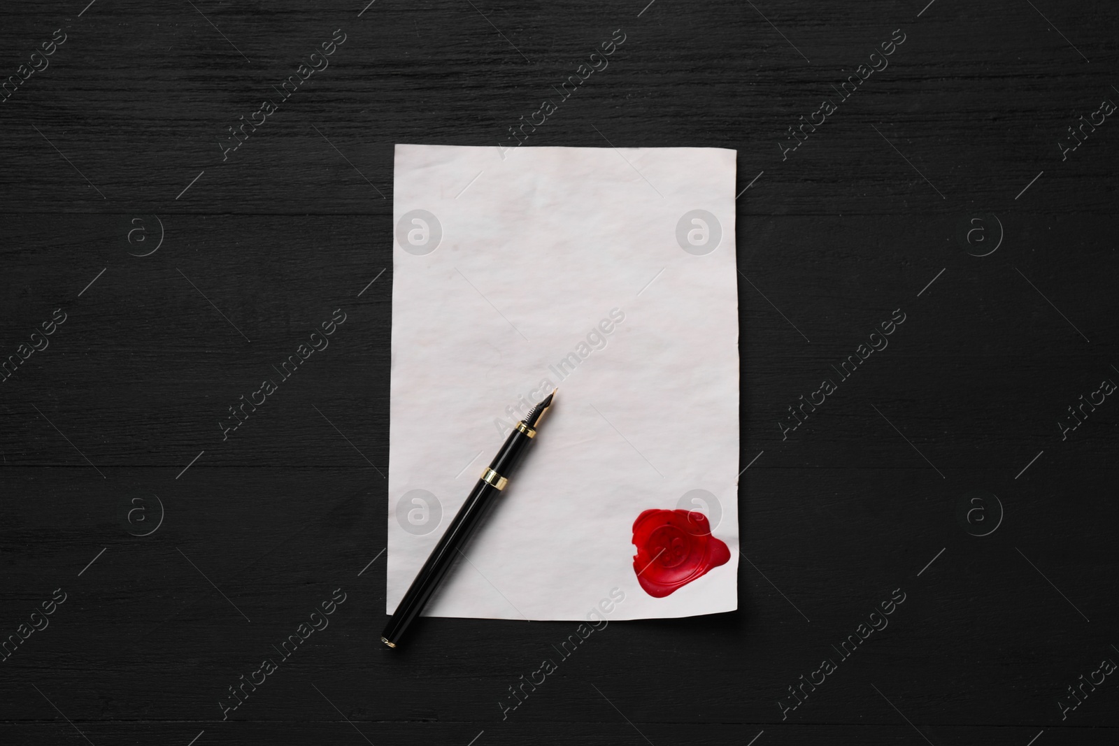 Photo of Old letter with wax stamp and fountain pen on black wooden table, top view