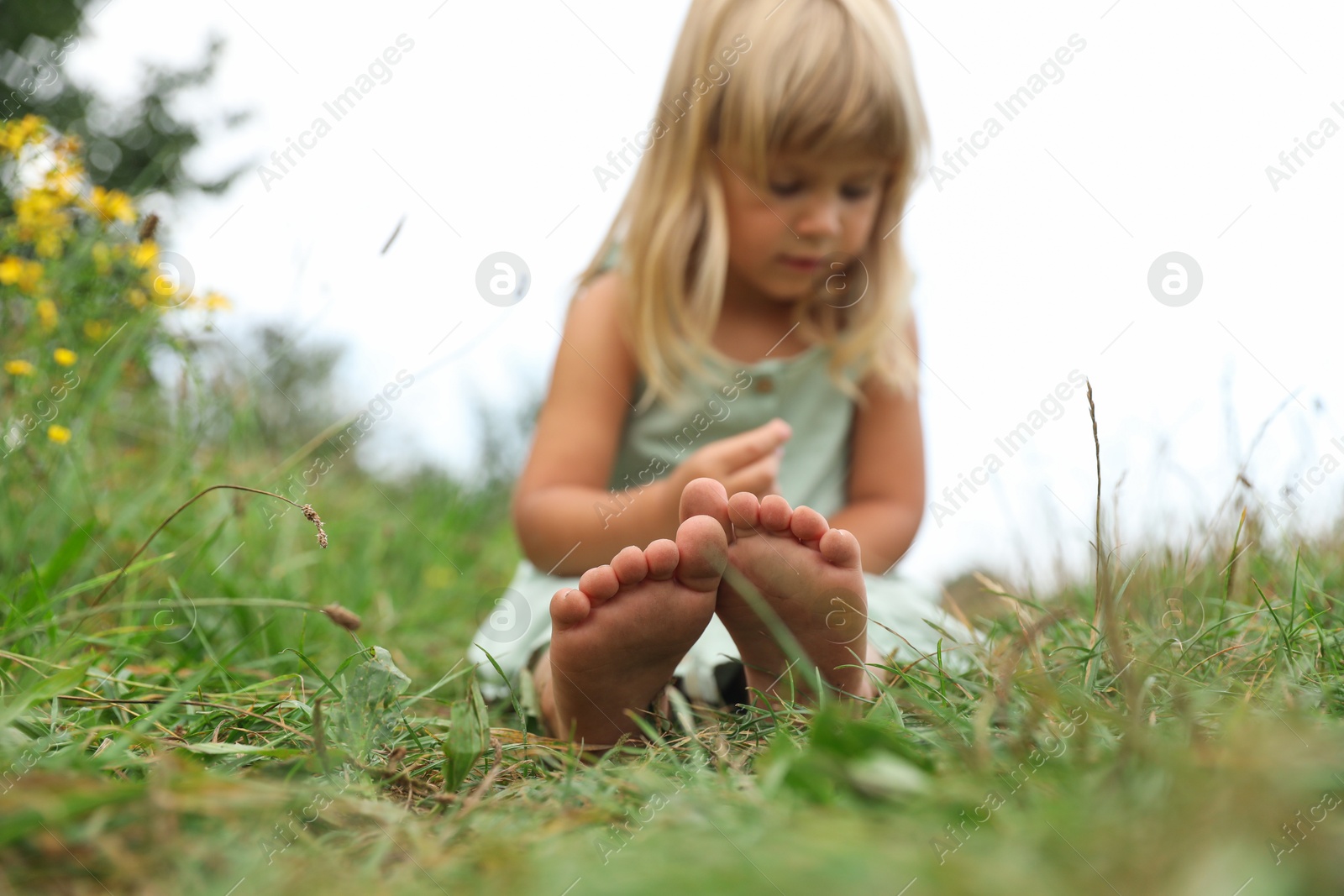 Photo of Barefoot little girl on green grass at meadow, selective focus. Child enjoying beautiful nature