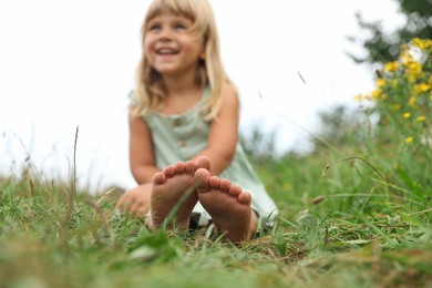 Photo of Barefoot little girl on green grass at meadow, selective focus. Child enjoying beautiful nature