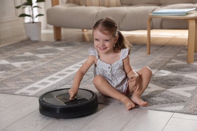 Photo of Cute little girl with robotic vacuum cleaner on floor at home