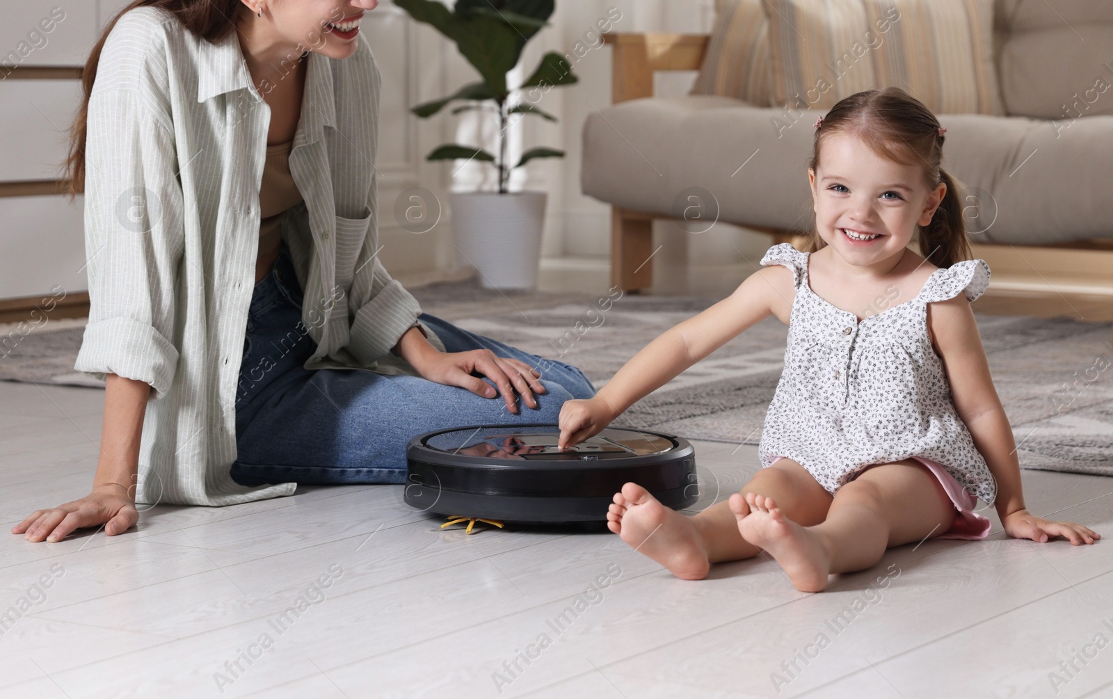 Photo of Mother and her daughter with robotic vacuum cleaner at home, closeup