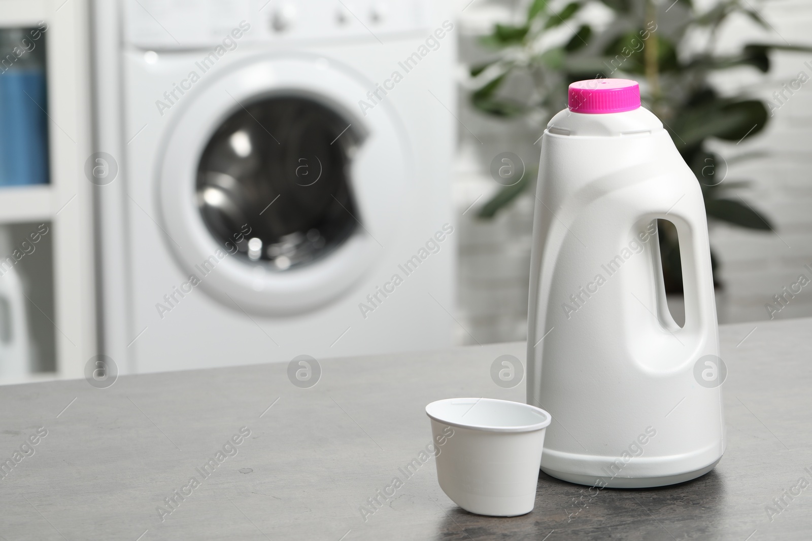 Photo of Laundry detergent and cap on grey table, space for text