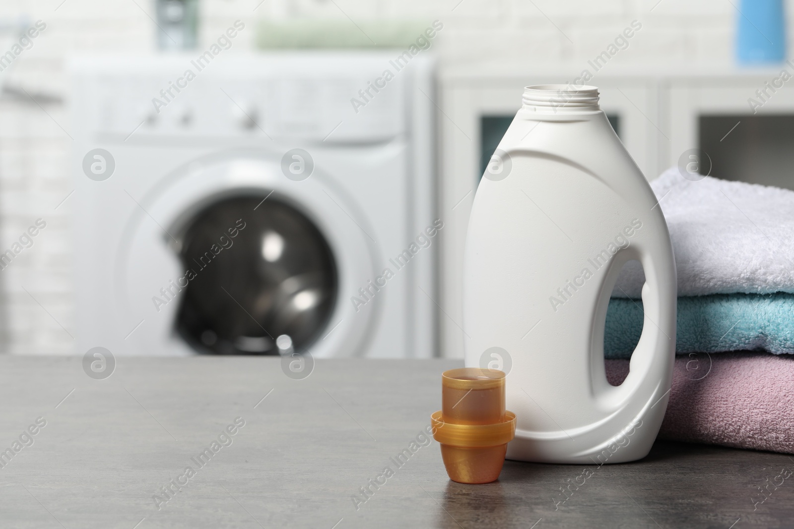 Photo of Laundry detergent, cap and stacked clean towels on grey table, space for text