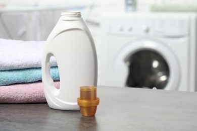 Photo of Laundry detergent, cap and stacked clean towels on grey table, space for text