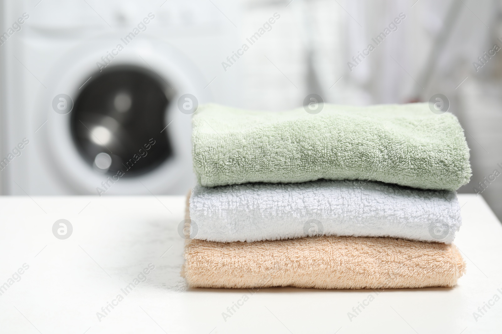 Photo of Stacked clean towels on white table in bathroom, space for text